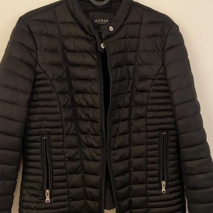 Svart quiltad jacka från Guess - Säljer en snygg svart quiltad jacka från Guess i mycket bra skick. Den har en dragkedja framtill och två praktiska fickor med dragkedjor. Perfekt för höst och vår, med en stilren design som passar till det mesta. Jackan är långärmad och har en normal passform.