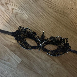 Svart spetsmask med pärlor - Snygg och elegant svart mask i spets med pärldetaljer. Perfekt för maskerad eller fest! Masken har ett intrikat mönster och sitter bekvämt med ett band runt huvudet. Den ger en mystisk och glamorös look. Priset kan alltid diskuteras 