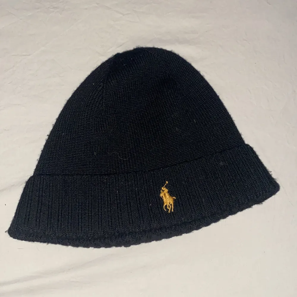 Snygg svart mössa från Polo Ralph Lauren i merinoull. Den har en diskret gul broderad logga framtill. Perfekt för kalla dagar och ger en stilren look. Mössan är i ett nytt skick och passar de flesta tack vare one size-storleken.. Accessoarer.