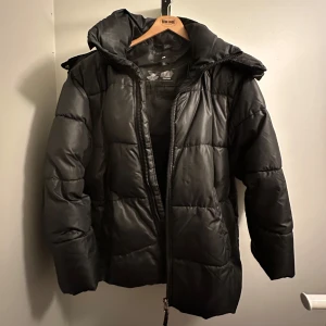 Svart pufferjacka - En svart pufferjacka från H&M i storlek S! Den har en dragkedja framtill och en praktisk huva. Perfekt för kalla vinterdagar. Den håller en otroligt varm på vintern!! 