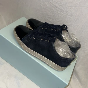 Mörkblå Lanvins - Säljer ett par snygga mörkblå sneakers från Lanvin i bra skick. Skorna har en stilren design med svarta lackdetaljer på tån och en vit sula. Perfekta för både vardag och fest! Kommer med originalkartong och dustbag.🍾🎧
