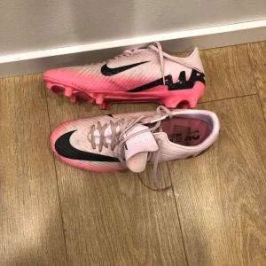Nike academy fotbollsskor i rosa och svart  - Säljer ett par Nike fotbollsskor i rosa och svart. De har en snygg design med svarta detaljer och snörning. Skorna är i bra skick och perfekta för fotbollsträning eller match. Sulan har bra grepp för gräsplaner. Skorn är använda 2 träningar och är i bra skick.