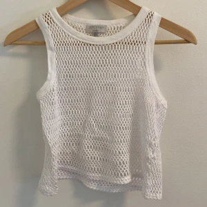 Vit nätlinne från Pull&Bear - Säljer ett snyggt vitt nätlinne från Pull&Bear. Perfekt för sommaren med sin luftiga design och ärmlösa stil. Linnet är gjort i ett syntetmaterial som ger en cool och trendig look. Passar perfekt till stranden eller en varm dag i stan! Så snygg att ha över en bikini eller på fest!