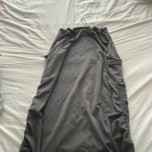 Grå långkjol med snörning - Säljer en snygg grå långkjol med coola snörningsdetaljer på sidorna. Kjolen har en bekväm passform och är perfekt för både vardag och fest. Den är gjord i ett mjukt material som känns skönt mot huden.