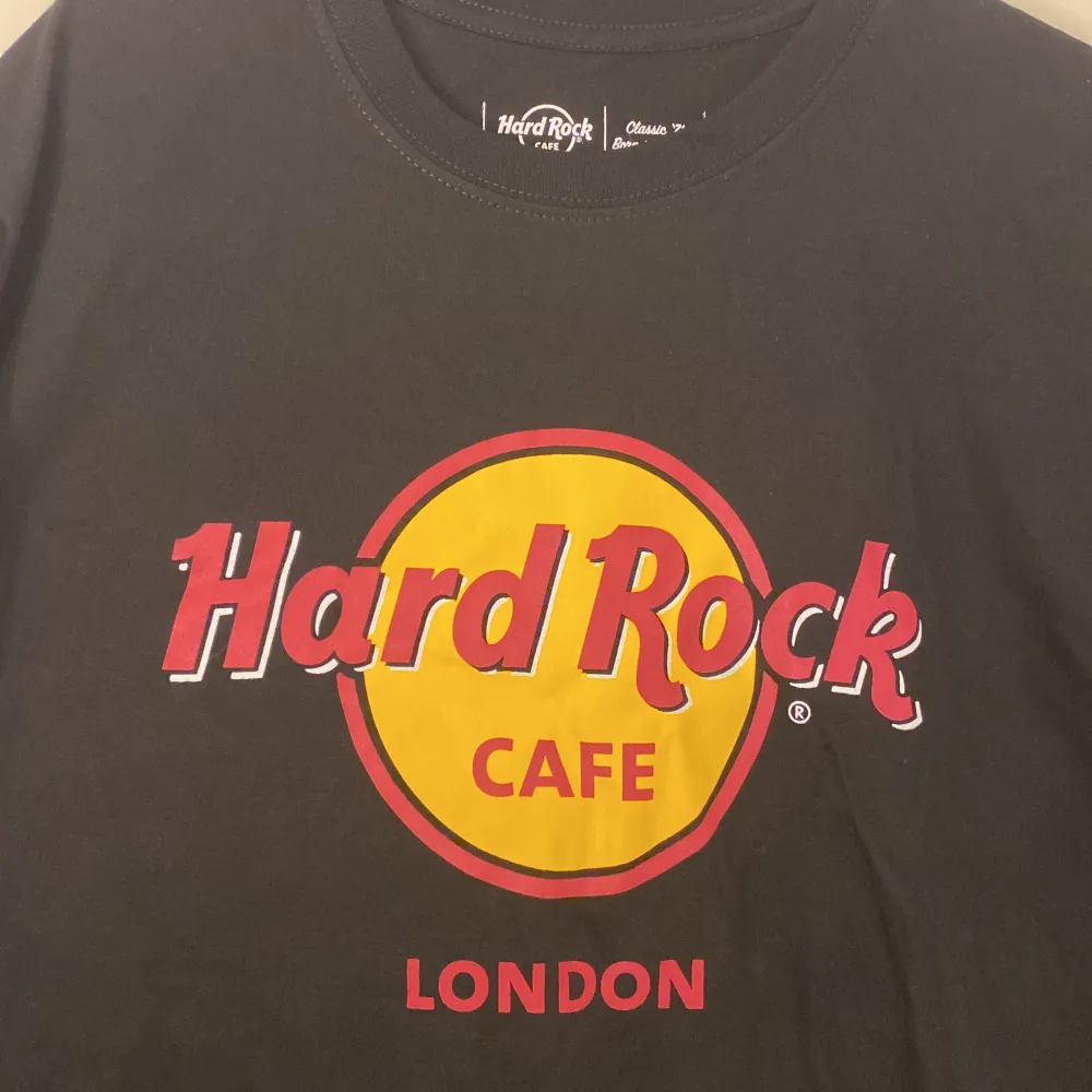 Säljer en klassisk svart T-shirt från Hard Rock Cafe i London. Den har det ikoniska Hard Rock Cafe-loggan i rött och gult på framsidan. T-shirten är i nyskick och har kvar prislapp. kvitto finns på bild 4 & priset i svenska kronor på Bild 5.. T-shirts.