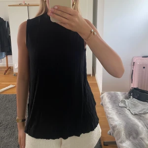 Svart ärmlös topp - Säljer en stilren svart ärmlös topp. Den är ribbad och lite lätt polo stil i kragen. 