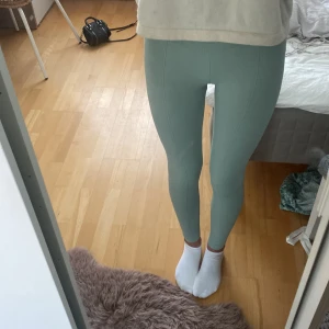 Gröna ribbade leggings - Säljer ett par gröna ribbade leggings i nyskick. De är högmidjade och har en tight passform, perfekt för träning. Materialet är mjukt och stretchigt, vilket gör dem superbekväma att ha på sig. Det finns en liten logga på baksidan. helt o andvändna!