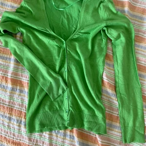 Grön kofta från Orsay - Säljer en snygg grön kofta från Orsay. Den har en v-ringad design med knappar framtill och långa ärmar. Perfekt för att lägga till lite färg i din garderob! 💚