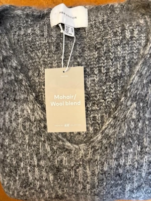Grå fluffig H&M Premium Stickad Mohairtröja Strl.M - Mysig grå stickad tröja med V-ringning och lång ärm. Tröjan har en fluffig, mjuk struktur och ett diskret mönster i garnet.                                         Helt ny med lappar kvar enligt bilder.  Strl. Medium (se mått bland bilderna)  Tillverkad i en mjuk och lyxig mohairmix  Nypris 1199kr  Se gärna mina övriga annonser för eventuell samfrakt!