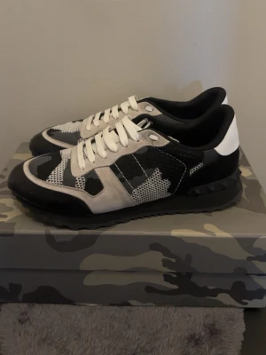 Valentino svartvita rockrunners - Snygga sneakers från Valentino i svart, vitt och grått med camomönster. Skorna har vita snören, svart sula och detaljer i mocka och mesh. Perfekta för dig som vill sticka ut med en unik och trendig look.