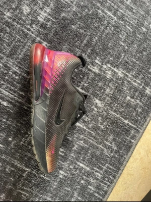 Nike Air Max svart/rosa sneakers - Säljer ett par Nike Air Max sneakers i svart med rosa och orange detaljer. Skorna har en synlig Air Max-sula i genomskinlig rosa, svarta snören och små prickdetaljer längs sidorna. Tillverkade i syntetmaterial och mesh för bra andningsförmåga.