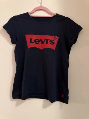 Mörkblå Levi's t-shirt med röd logga - Snygg mörkblå t-shirt från Levi's med den klassiska röda loggan tryckt framtill. T-shirten har rund halsringning och korta ärmar.