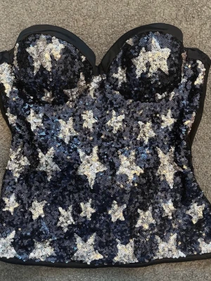Paljettprydd bustier från Intimissimi - Supersnygg bustier från Intimissimi täckt med svarta och silvriga paljetter i stjärnmönster. Axelbandslös modell med vadderade kupor och markerad byst. Perfekt för dig som vill sticka ut och älskar glitter och glam.