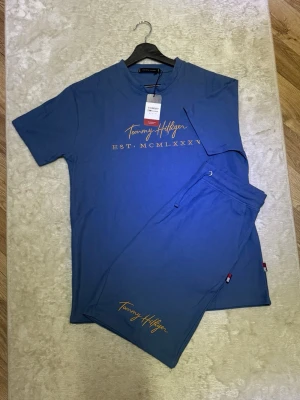 Blått set från Tommy Hilfiger - Snyggt blått set från Tommy Hilfiger med t-shirt och shorts. Helt ny med prislappen kvar, storlek L men passar även M. Perfekt om man vill ha en toppad outfit en varm sommarkväll.