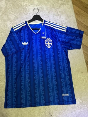 Blå Sverige tröja från Adidas - Säljer en blå Sverige fotbollströja från Adidas, prislappen kvar samt alla klistermärke så mer ny går ej att hitta. Storlek L passar även M. Perfekt för en varm sommarkväll eller bara till ett träningspass på gymmet. Tveka ej på att höra av dig!
