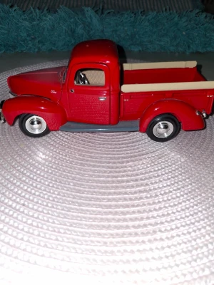 Röd modellbil pickup i metall - Säljer en detaljerad röd modellbil av en klassisk pickup med silverfärgade hjul och beige inredning. Bilen är tillverkad i metall och plast, har öppningsbara dörrar och realistiska detaljer som kromade fälgar och träliknande sidor på flaket.