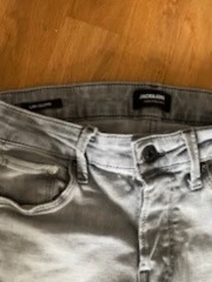 Ljusgrå jeans från Jack & Jones strl xs - Säljer ett par ljusgrå jeans från Jack & Jones med klassisk femficksmodell och raka ben. Jeansen har bälteshällor och knappgylf. Perfekta för dig som gillar en clean och stilren look. Djur och rökfri hem