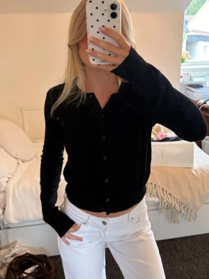 Svart basic cardigan med knappar - En svart, långärmad cardigan med knäppning framtill. Modellen är enkel och rak med rund halsringning och smala muddar vid ärmslut och nederkant. Perfekt att slänga över en topp för en clean look.