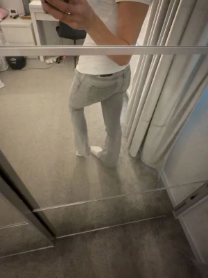 Ljusgrå bootcut jeans - Säljer ett par ljusgrå bootcut jeans och klassisk femficksdesign. Jeansen har normal midja och är tillverkade i ett mjukt denimtyg som sitter snyggt på benen. Perfekta för en clean och stilren look.
