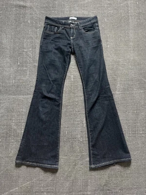 Mörkblå bootcut jeans med kontrastsömmar - Snygga mörkblå bootcut jeans med vita kontrastsömmar och klassisk femficksmodell. Jeansen har låg midja och vida ben som ger en retrovibe. Perfekta för dig som gillar en avslappnad men trendig stil. Från Gina Tricot i storlek 36.