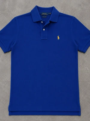 Blå pikétröja från Polo Ralph Lauren - Klassisk blå pikétröja från Polo Ralph Lauren med gul broderad logga på bröstet. Tröjan har korta ärmar, krage och två knappar framtill. Perfekt till jeans eller shorts för en clean och stilren look.