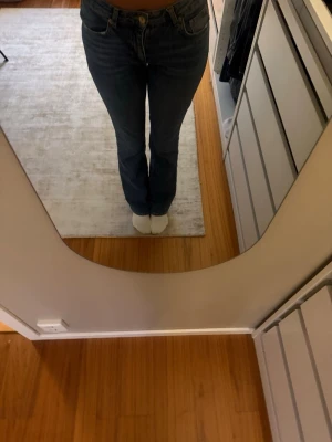 Mörkblå bootcut jeans - Säljer ett par mörkblå bootcut jeans med klassisk femficksdesign och hög midja. Jeansen har raka ben som smalnar av något vid knäna och sedan blir vidare nedtill. Perfekta till en avslappnad och trendig look.