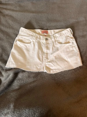 Vita jeansshorts från ONLY - Säljer ett par vita jeansshorts från ONLY med rå kant nertill och klassisk femficksdesign. Shortsen har knapp och dragkedja framtill samt bälteshällor. Perfekta för varma dagar och ger en fräsch look.