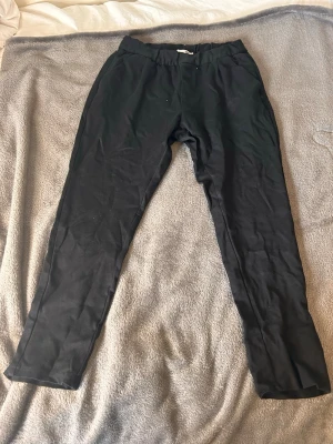 Svarta mjukisbyxor med resårmidja - Svarta mjukisbyxor med resår i midjan och raka ben. Byxorna har en enkel och clean look, perfekta för chill dagar hemma eller när du vill vara bekväm. Tillverkade i mjukt material som känns skönt mot huden. Passar dig som gillar en avslappnad stil.