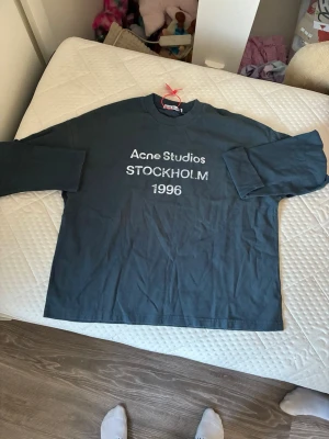 Mörkblå långärmad topp Acne Studios - Snygg mörkblå långärmad topp från Acne Studios med tryck 'STOCKHOLM 1996' framtill. Klassisk rund halsringning och relaxed fit. Perfekt till jeans eller kjol för en cool och enkel look.