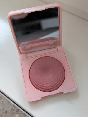 CAIA Raspberry Passion rouge  - Säljer ett puderrouge från CAIA i en snygg rosa nyans. Rouget kommer i en stilren, ljusrosa fyrkantig dosa med spegel i locket och har en rundad, upphöjd form. Perfekt för att ge kinderna en fräsch färg och glow.