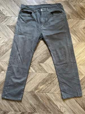 Levi's 505 - Säljer ett par grå jeans från Levi's med klassisk rak passform och fem fickor. Jeansen har en diskret tvätt och tydliga sömmar, samt Levi's ikoniska läderpatch bak i midjan. Perfekta för en avslappnad och stilren look. Längd 102cm Bredd 43cm