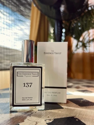 The Essence Vault 137 Eau de Parfum, 30ml - The Essence Vault 137 Eau de Parfum kommer i en stilren, genomskinlig glasflaska med silverfärgad kork och svartvit etikett. Doften är elegant förpackad och flaskan har en modern, fyrkantig form. Medföljer gör en matchande vit kartong med minimalistisk design.Ny, bara testad