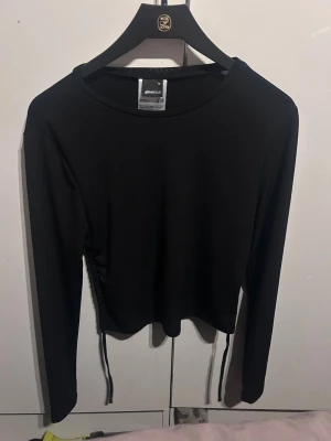 Svart långärmad topp med snörning - Svart långärmad topp från Gina Tricot med snörning i sidorna och öppen rygg. Modellen är croppad och har en tight passform. Perfekt för dig som gillar trendiga och stilrena plagg.
