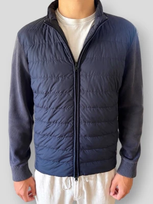 Woolrich Bomber Cardigan - Woolrich Bomber Cardigan | Modell: Hybrid Bomber Jacket | Färg: Marinblå (Navy) | Material: Mjuk premium bomull med vindavvisande, lätt fodrad framsida | Skick: Fint skick i övrigt men det stickade tyget på ärmar/axlar har blivit lite solblekt men inget man tänker på (se bilder) | Nypris: 3999 kr | Storlek: M (Normal i storleken / True to size) | Hör av dig vid minsta fundering 📦