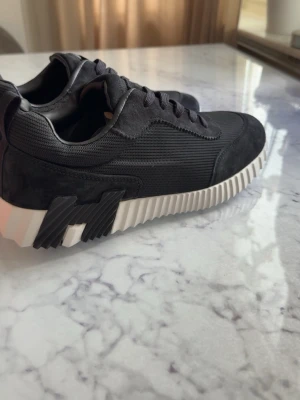 Svarta sneakers med vit sula - Snygga svarta sneakers med en chunky, räfflad vit sula och detaljer i mocka och mesh. Skorna har svarta skosnören och en cool kontrastdetalj på sidan. Perfekta för dig som gillar en modern och sportig look.
