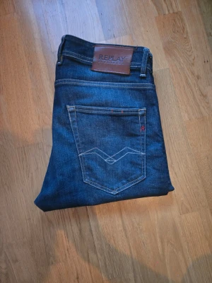 Mörkblå jeans från Replay - Snygga mörkblå jeans från Replay med klassisk femficksmodell och kontrastsömmar. Jeansen har en skinnpatch med logga bak i midjan och diskreta slitningar framtill. Perfekta för en trendig och avslappnad stil. Mycket bra skick 