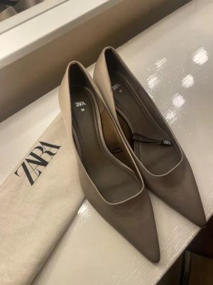 Beige pumps med låg klack från Zara - Stilrena beige pumps från Zara med spetsig tå och låg klack. Skorna har en elegant och enkel design som passar till många olika looks. Tillverkade i ett mjukt material med matt finish och kommer med en matchande dustbag.