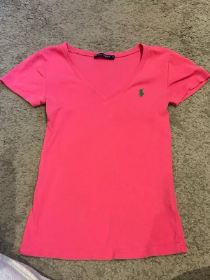  t-shirt  - Snygg rosa t-shirt från Ralph Lauren med v-ringning och klassisk grön logga broderad på bröstet. T-shirten är kortärmad, köpt second hand men den set som ny ut!💗💗