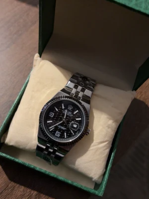 Klassisk silverfärgad klocka - Stilren klocka i silverfärgat metallarmband och svart urtavla med tydliga siffror och datumvisning. Klockan har en klassisk design och passar perfekt till dig som gillar tidlösa accessoarer.