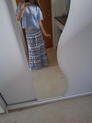 Blåvit långkjol från Gina Tricot - Säljer en blåvit långkjol från Gina Tricot med ett snyggt mönster och elastisk midja. Kjolen har ett flowy fall och passar perfekt till sommaren. Superenkel att matcha med en crop top eller t-shirt!