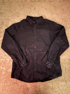 Marinblå  linneskjorta från Cubus  - Snygg marinblå skjorta i linne- och bomullsblandning. Klassisk krage, långa ärmar med manschetter och knappar framtill. En bröstficka ger en clean look. Perfekt till jeans eller chinos för en avslappnad stil.