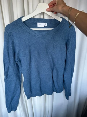 Blå stickad tröja från VILA - Mysig blå stickad tröja från VILA med rund halsringning och långa ärmar. Tröjan har ribbade muddar vid ärmslut och nederkant, vilket ger en klassisk och enkel look. Perfekt att matcha med jeans eller kjol.