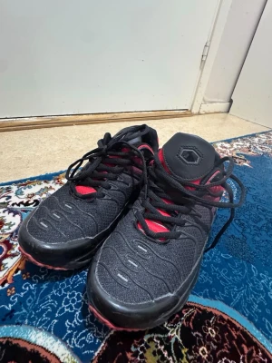 Svarta och röda sneakers med mönster - Snygga sneakers i svart och rött med coola vågmönster på sidan och meshdetaljer. Skorna har svarta snören, vadderad plös och sula med luftbubblor för extra komfort. Passar perfekt till streetwear och har en modern look.