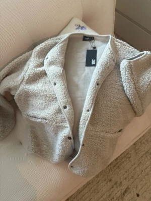 Beige teddyjacka från 157 - Mysig beige teddyjacka från 157 i storlek M. Jackan har tryckknappar framtill, och två stora fickor, 