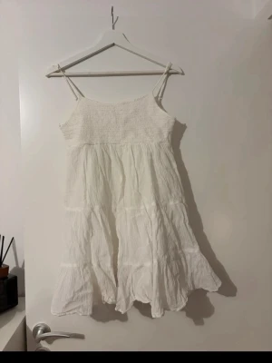 Vit sommarklänning med volang - Luftig vit klänning med smala axelband och volangig nertill. Perfekt för varma dagar och enkel att styla med accessoarer.