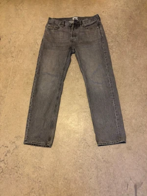 Grå  jeans - Säljer ett par grå jeans med klassisk rak passform. Jeansen har normal midja och stängs med dragkedja och knapp. Materialet är denim i bomull och färgen är en snygg tvättad grå nyans. Bredd 30 och längd 32