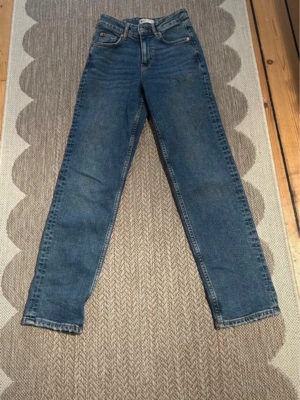 Blå raka jeans med hög midja - Säljer ett par klassiska blå jeans med rak passform och hög midja. Jeansen har fem fickor, bälteshällor och stängs med knapp och dragkedja. Perfekta till vardags och passar till det mesta. Materialet är denim i bomull.