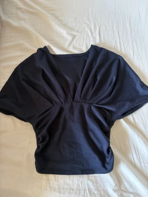 Mörkblå v-ringad topp med kort ärm - Snygg mörkblå topp med v-ringning. Toppen har en croppad passform och markerad midja som ger en cool siluett. Köpt secondhand utan några lappar men passa storlek s💕