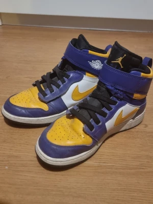 Nike Air Jordan 1 Lakers färg - INSTABOX!!! TVÄTTAS VID KÖPET. Säljer ett par Nike Air Jordan 1 sneakers i Lakers-inspirerad färgkombination med gult, lila och vitt. Skorna har högt skaft, svart plös och snörning samt kardborreband upptill. Klassisk Swoosh-logga i gult på sidan och Air Jordan-märke på ankeln.