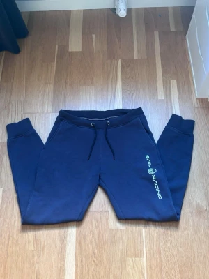  Sail Racing byxor  - Snygga marinblå mjukisbyxor från Sail Racing med logga längs benet. Byxorna har dragsko i midjan, muddar vid bensluten och två sidofickor. Perfekta för chill dagar eller när du vill ha det bekvämt.